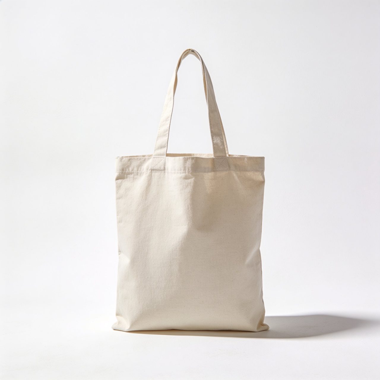 Plain off-white cotton canvas tote bag with shoulder straps standing upright against a white background.